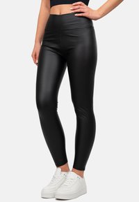 Leggings neri in ecopelle con vita alta, texture liscia e design aderente, abbinati a sneaker bianche.