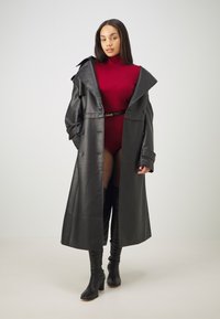 Čierny kožený dlhý kabát s oversized golierom, v kombinácii s priliehavým červeným body a čiernymi vysokými podpätkami s ponožkami s bodkami.