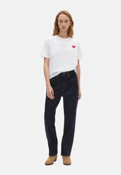 Hvid bomulds t-shirt med rød hjertegrafik på venstre bryst, parret med mørkeblå denim jeans og lysebrune ankelstøvler.