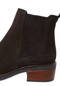 Stivaletto in camoscio nero con pannelli elastici laterali, punta arrotondata e tacco in legno impilato. Finitura texture con dettagli di cucitura sottili.