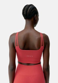 Reggiseno sportivo rosso con spalline sottili, realizzato in tessuto testurizzato, con un logo sul retro e un design aderente per l'abbigliamento attivo.