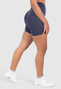 Bermudas de talle alto en color azul marino, hechas de un tejido elástico, con costuras que contornean la figura y una textura suave, combinadas con zapatillas y calcetines blancos.