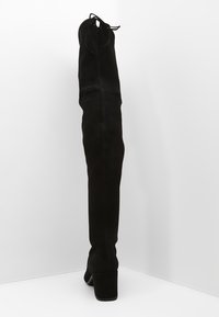 Bota de ante negra por encima de la rodilla con punta redonda, tacón cuadrado y lazo ajustable en la parte superior para un ajuste seguro. Textura suave con detalle de costura.