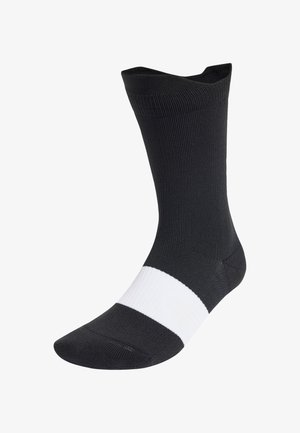 Chaussettes noires côtelées avec une bande horizontale blanche au milieu. Fabriquées en matériau doux et extensible. Design à la cheville.