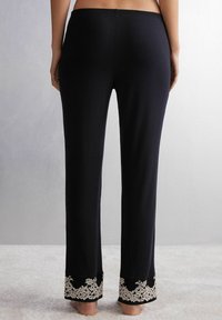 Zwarte pantalons met een rechte snit, voorzien van een delicate kantafwerking in een bloemenpatroon aan de zoom. Zacht materiaal met een elastische tailleband.