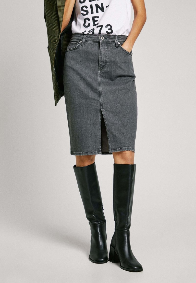 Donkere grijze denim kokerrok met een voorste split, ontworpen met een taille tot halverwege en een vijfzakkenstijl. Gecombineerd met kniehoge zwarte laarzen.