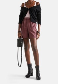 Mustapaitainen neuletakki, vaaleanpunainen toppi, ruutukuosiset shortsit ja mustat korokepopot. Asusteina pieni musta laukku, jossa on tekstuuri.