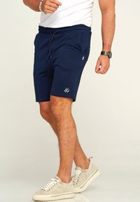 Marineblaue Shorts aus weichem Stoff, mit elastischem Bund, seitlichen Taschen und einem weißen Logoakzent am Saum.