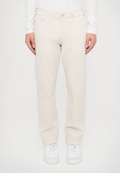 Pantalons en coton beige clair avec une coupe droite, cinq poches, et une texture subtile. Associés à des baskets blanches.