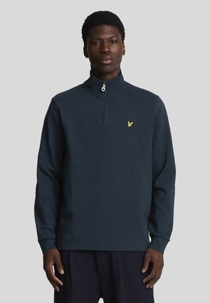 Pullover a quattro zip di colore blu navy realizzato in tessuto morbido, con maniche lunghe e un piccolo logo di un'aquila gialla sul petto.