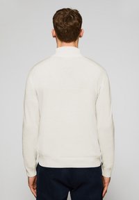 Sudadera de crema clara con manga larga, puños y dobladillo acanalados, cuello plano, textura suave y un detalle minimalista en los hombros.