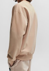 Sudadera de color beige claro con puños y dobladillo acanalados, que presenta un corte relajado y un material suave, mostrada de lado.