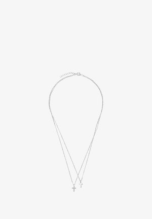Srebrny podwójny naszyjnik z dwoma małymi medalionami w kształcie krzyża, z których jeden ozdobiony jest akcentem kamieni, połączonymi delikatnym łańcuszkiem. Z regulowanym zapięciem.