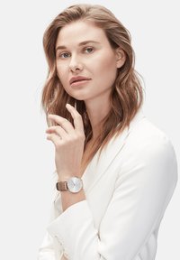 Ronde horloge met een witte wijzerplaat en zilveren uurmarkeringen. Heeft een kast van roségoud en een gestructureerde roségouden mesh band.