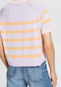 Eine Person trägt ein kurzärmliges Strickoberteil mit pastell-lila und orangefarbenen horizontalen Streifen sowie eine blaue Jeans, von hinten gezeigt.