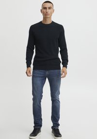 Pulover tricotat navy cu guler rotund, asortat cu blugi albastri skinny și teniși negri. Textură netedă, design simplu.