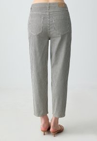 Pantaloni a righe a vita alta con una vestibilità ampia, dotati di chiusura con bottone, due tasche posteriori e un tessuto testurizzato in bianco e nero.