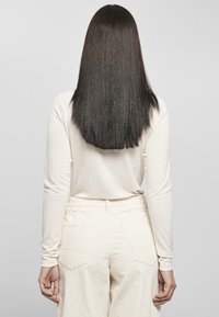 Top crema a maniche lunghe abbinato a pantaloni in velluto a coste crema a vita alta. Capelli lisci, scuri, che superano le spalle.