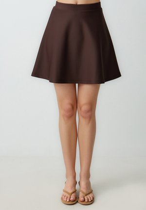 Gonna a ruota marrone in tessuto liscio con design svasato. Presenta una vita alta e arriva sopra il ginocchio, abbinata a infradito color beige.