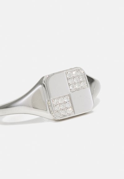 Ezüst gyűrű, négyzet alakú felső résszel, melyben két szakaszban átlátszó strasszkövek vannak beágyazva, sima szalaggal és fényes felülettel.