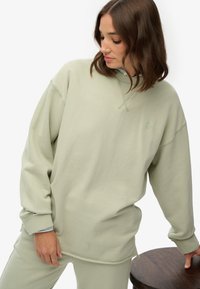 Jasnozielona, oversize bluza z teksturowanym wykończeniem, z okrągłym dekoltem i ściągaczami na mankietach. Haftowane logo na piersi.