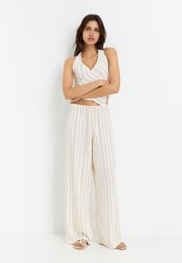 Top halter leggero di colore crema con un design avvolto, abbinato a pantaloni larghi e svasati con righe verticali. Tessuto morbido.