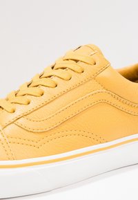 Gele lederen sneaker met een gestructureerd oppervlak, opvallende stiksels, vetersluiting en een witte rubberen zool met een gele accentstreep.