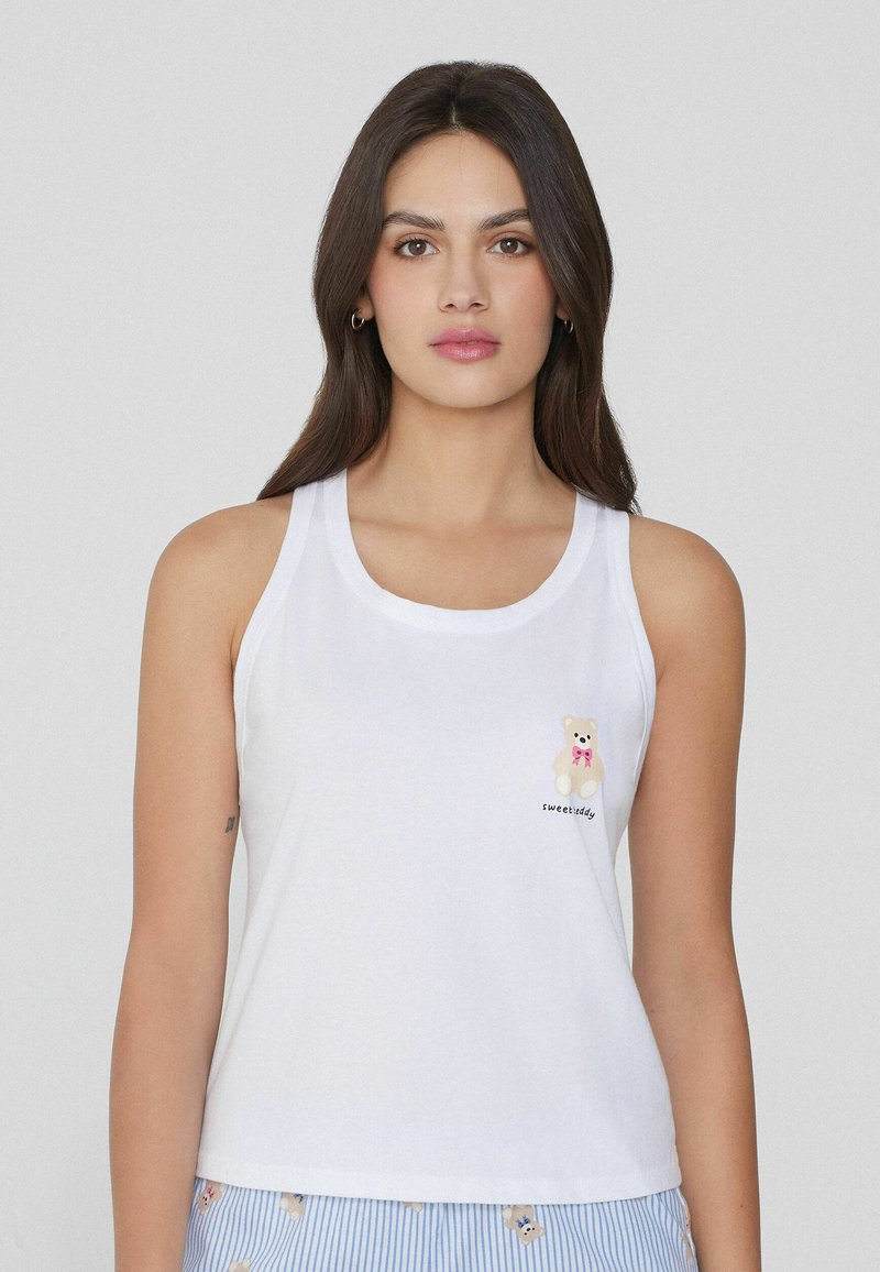 Camiseta sin mangas blanca de algodón con un escote redondeado. Presenta un diseño bordado de un oso y el texto "sweetiddy" debajo.