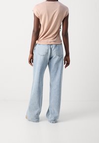 Camiseta rosa clara con mangas enrolladas, combinada con jeans de pierna ancha de color azul claro que tienen bolsillos traseros y un ajuste relajado.