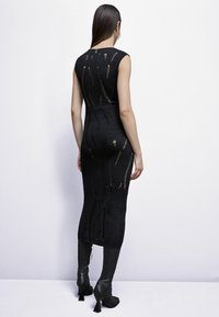 Abito nero a maglia con una silhouette aderente, caratterizzato da linee verticali, dettagli cut-out e lunghezza a metà polpaccio. Abbinato a stivali neri con tacco.