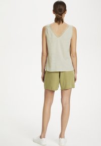 Top senza maniche verde chiaro con finiture in pizzo sul collo, abbinato a pantaloni corti verde oliva. Modella con scarpe da ginnastica bianche.