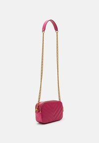 Borsa a tracolla trapuntata rosa con motivo a zigzag, dotata di una tracolla a catena dorata e chiusura con zip. Forma rettangolare compatta.