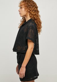 Schwarzes gehäkeltes Zweiteiler-Set mit einem kurzärmligen, cropped Top mit Kragen und einem hoch taillierten Rock. Filigranes Spitzendesign im gesamten Set.