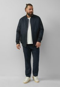 Marine bomberjack met een rits, twee zijzakken, geribbelde manchetten en een effen wit T-shirt, gecombineerd met marineblauwe broek en witte sneakers.