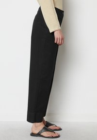 Černé bavlněné kalhoty se rovnou siluetou, s knoflíkovým zapínáním a bočními kapsami. Nošeny s černými žabkami.