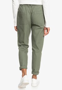 Chinos en coton vert à coupe décontractée, avec deux poches arrière et revers retroussés, assortis à des baskets blanches.