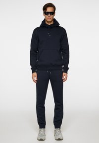 Mørkeblå sweatshirt med snørehætte og lommer foran, parret med matchende stramme sweatpants og bæres med grå sneakers.