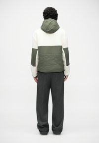 Jachetă căptușită cu un design în blocuri de culori alb și verde măsliniu, având glugă și textură matlasată, asortată cu pantaloni largi de culoare gri închis.