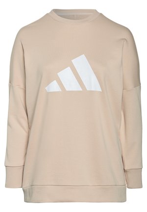 Person iført en beige langærmet sweatshirt med et stort hvidt Adidas-logo, kombineret med mørke bukser, beskåret ved hoved og knæ.