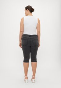 Pantalones capri de mezclilla negra con un ajuste slim, cintura de media altura, dos bolsillos traseros y dobladillo plegado, combinados con una blusa blanca sin mangas.