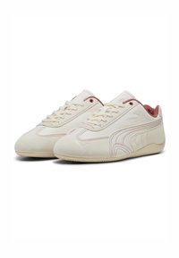 Zapatillas de cuero blancas con detalles en rosa, superficie lisa, punta redondeada y suela texturizada que presenta el logo de Puma en un lado.