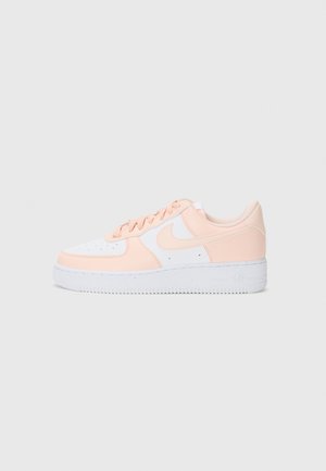 Lavtopsneakers i hvid og lys fersken med snørebånd, perforeret tå og tyk hvid sål på en ensfarvet lysegrå baggrund.