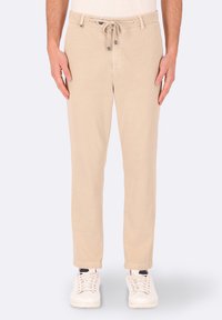 Pantaloni beige leggeri con vita regolabile e tasche frontali. Design a gamba dritta con una texture liscia, abbinati a sneakers bianche.