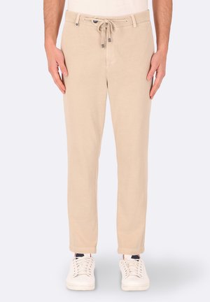 Pantaloni beige leggeri con vita regolabile e tasche frontali. Design a gamba dritta con una texture liscia, abbinati a sneakers bianche.