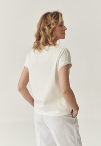 Haut blanc à manches courtes avec un col rond et une bordure en tricot texturé aux manches. Matériau en coton lisse, affiché en vue de profil.