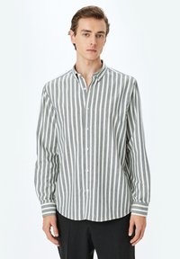 Camisa de algodón a rayas en gris y blanco, con botones en la parte delantera, cuello clásico, mangas largas, con rayas verticales y puños con banda.