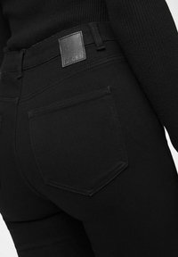 Svart denimjeans med strukturert finish, med en firkantet lærpatch på midjebåndet og dobbel baklomme med sømdetaljer.
