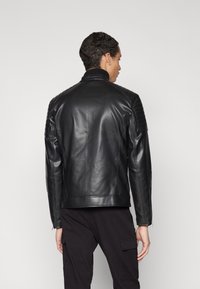 Black leather jacket with ribbed shoulder detailing, slim fit, and zippered cuffs. Smooth texture, classic collar, and minimalistic design.