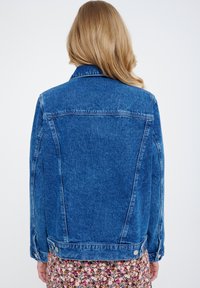 Giacca in denim blu lavato con colletto classico, maniche lunghe e dettagli sui bottoni. Presenta un design pulito sul retro senza decorazioni.