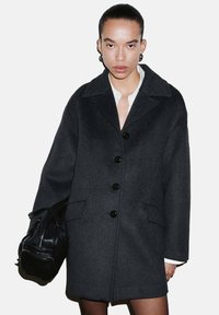 Abrigo de lana color carbón con solapa de muesca, cinco botones negros, bolsillos laterales y ajuste relajado. Textura suave y diseño minimalista.